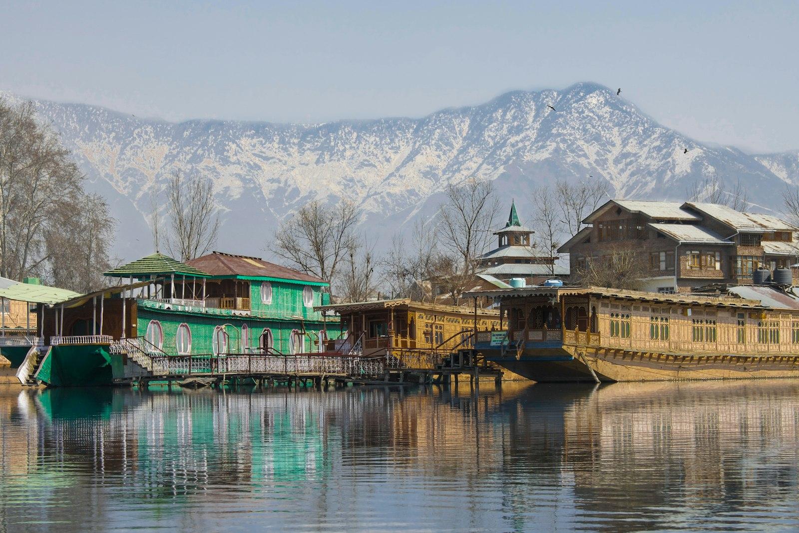 Shikara boats on a calm lake in Kashmir surrounded by mountains